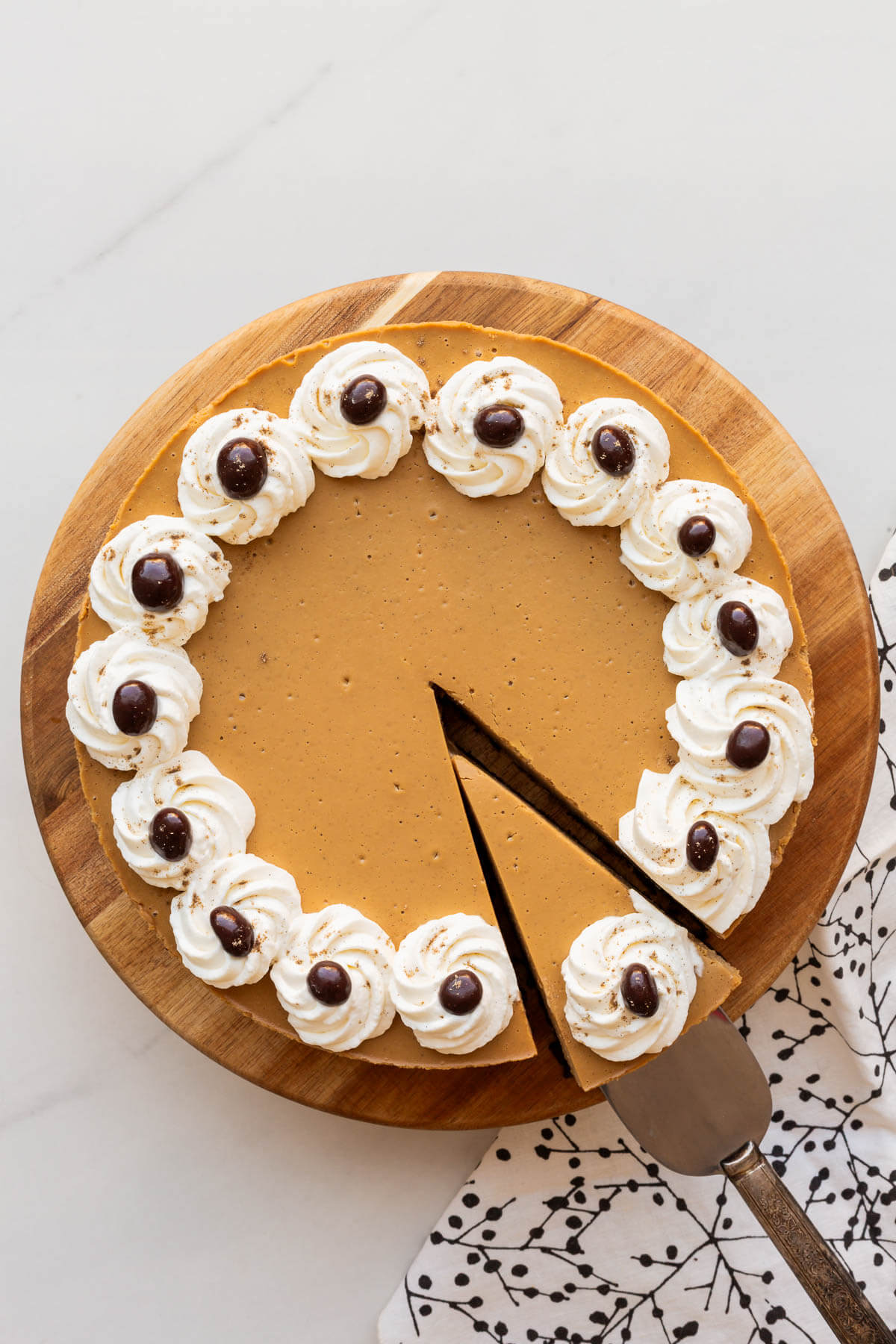 Serving a slice of coffee cheesecake that is decorated with a border of rosettes of whipped cream and chocolate covered coffee beans.