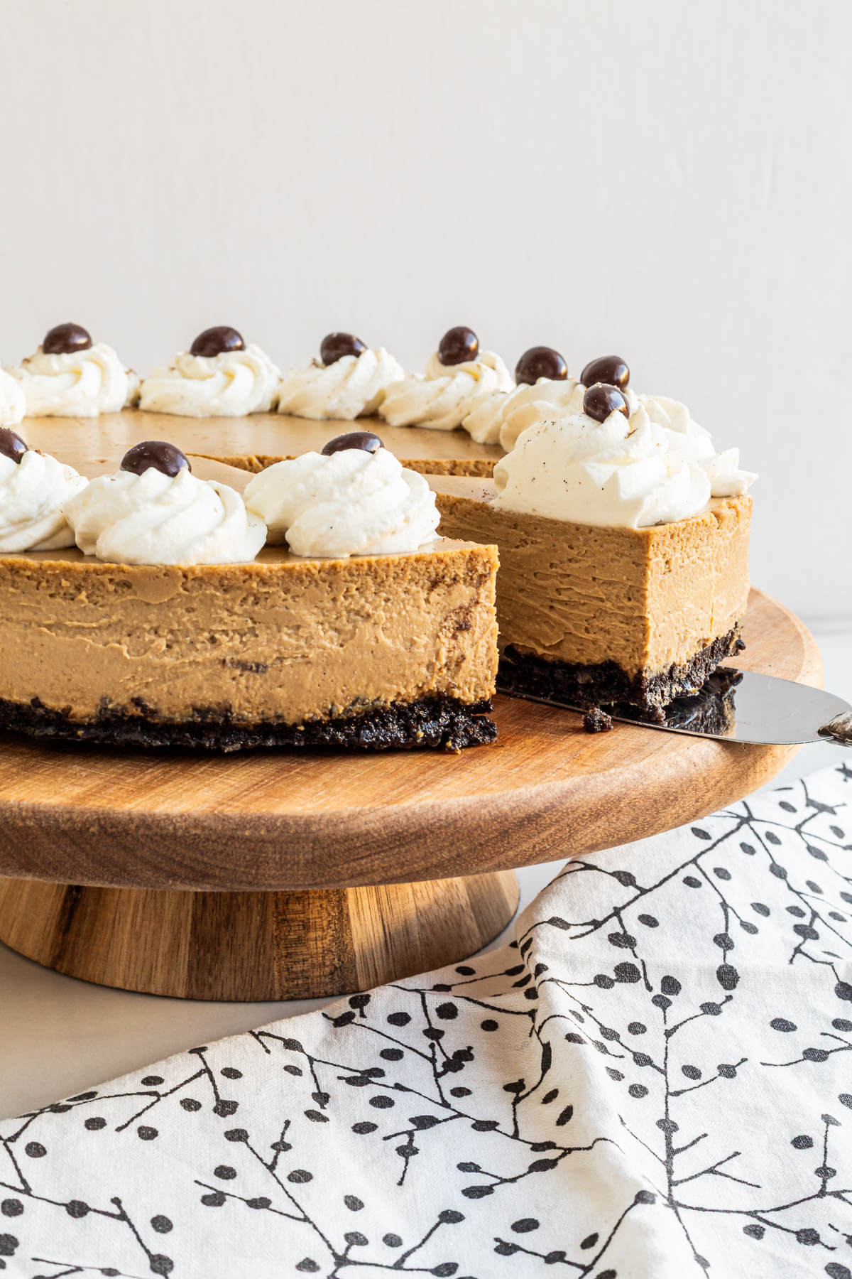 Serving a slice of a coffee cheesecake with a chocolate cookie crust and decorated with whipped cream and chocolate-covered coffee beans.