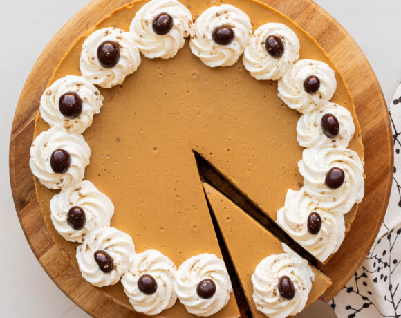 Serving a slice of a coffee-flavoured cheesecake with whipped cream piped around the border and chocolate-covered coffee beans.