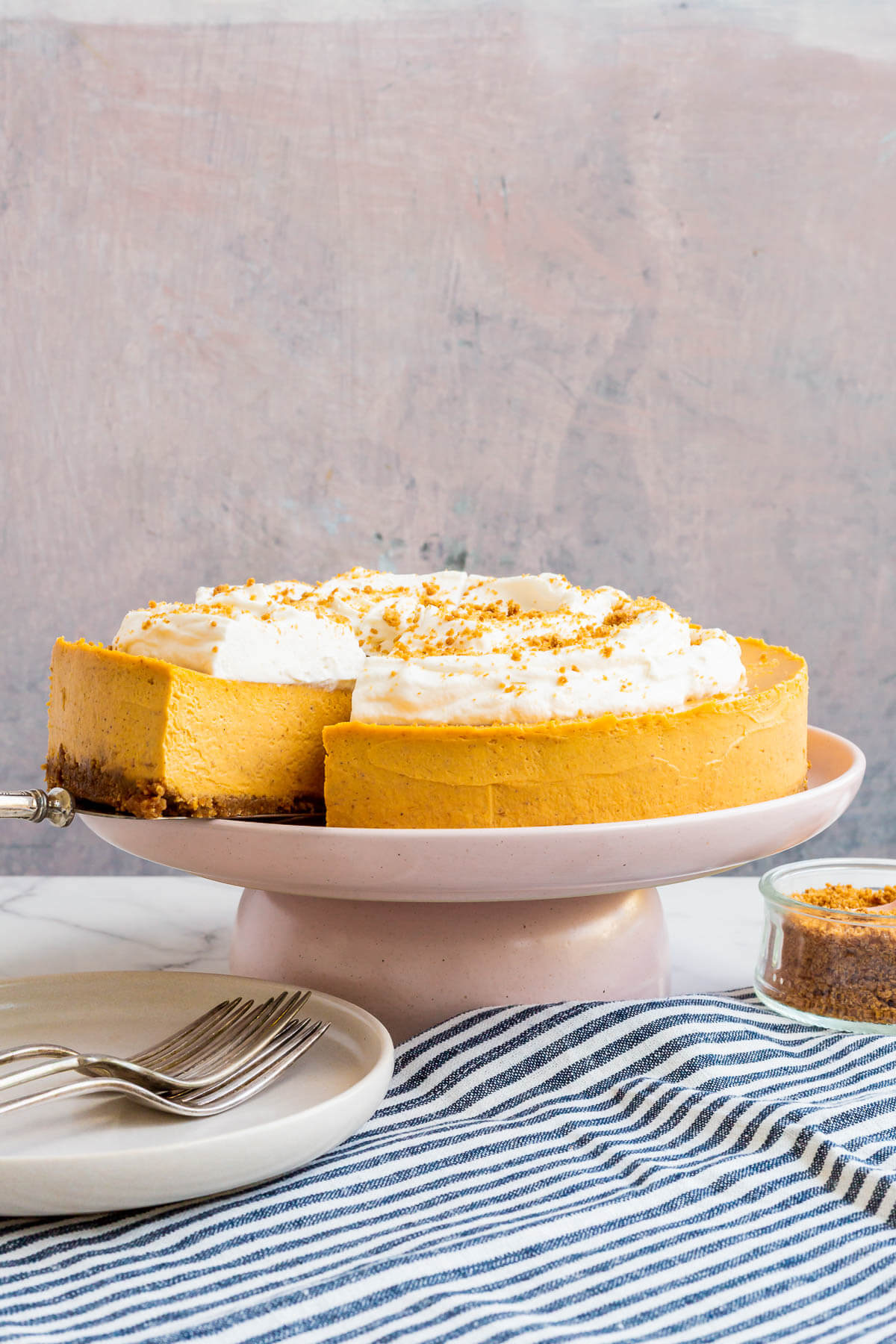 Serving a pumpkin cheesecake with a graham cracker crumb crust and topped with whipped cream