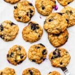 Blueberry oatmeal cookies with white chocolate and golden brown edges, freshly baked on a parchment paper-lined sheet pan.