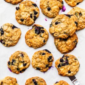 Blueberry oatmeal cookies with white chocolate and golden brown edges, freshly baked on a parchment paper-lined sheet pan.