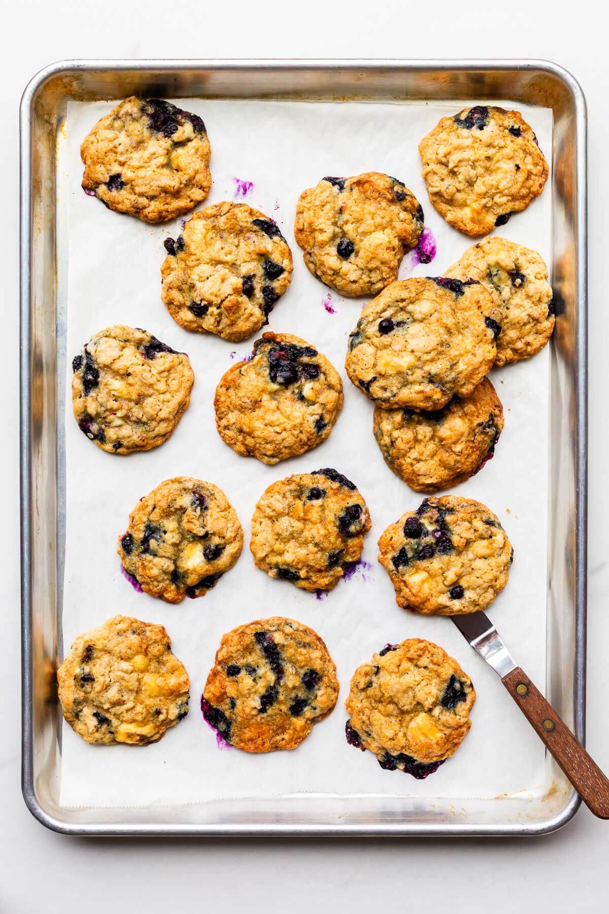 Blueberry white chocolate oatmeal cookies on a sheet pan after baking until the edges are golden brown and set.