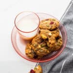 A glass of milk served with apple butter, cranberry, white chocolate chip cookies.