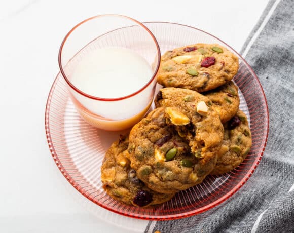 A glass of milk served with apple butter, cranberry, white chocolate chip cookies.