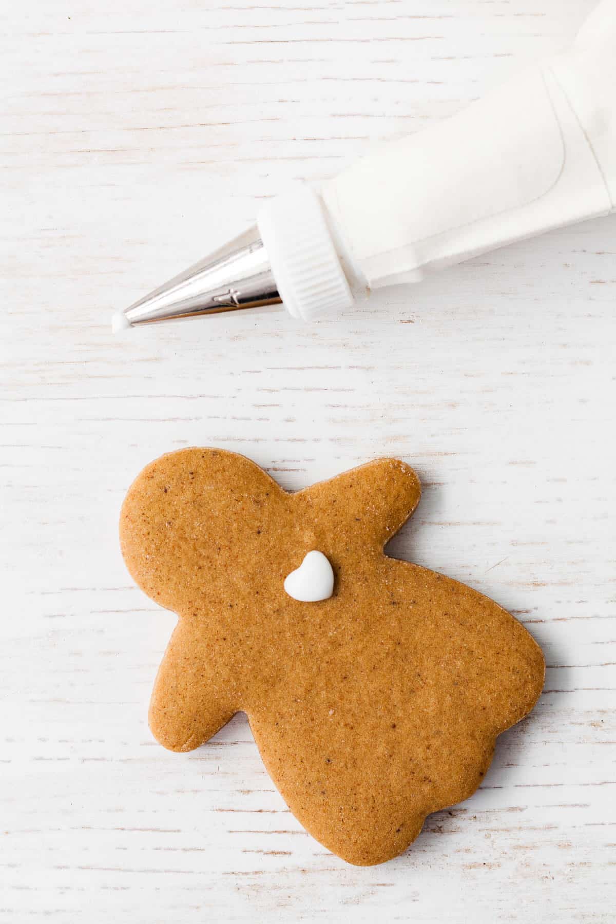 A cutout gingerbread cookie person with a heart of icing piped on with royal icing.