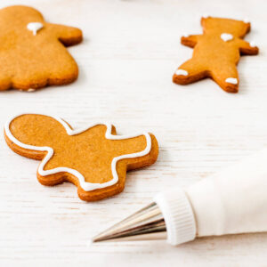 Using a piping bag fitted with a fine, small round tip to outline and decorate cutout gingerbread cookies with royal icing.