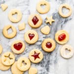 Homemade jam-filled shortbread cookies with little cutout windows shaped like hearts and stars.