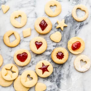 Homemade jam-filled shortbread cookies with little cutout windows shaped like hearts and stars.