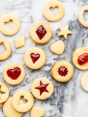 Homemade jam-filled shortbread cookies with little cutout windows shaped like hearts and stars.