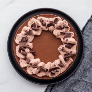 A gorgeous chocolate cheesecake decorated with swirls of whipped cream and shards of dark chocolate.
