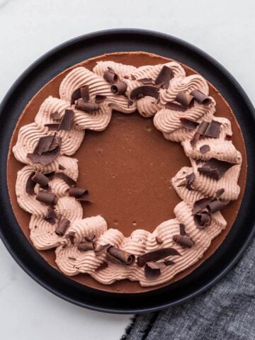 A gorgeous chocolate cheesecake decorated with swirls of whipped cream and shards of dark chocolate.