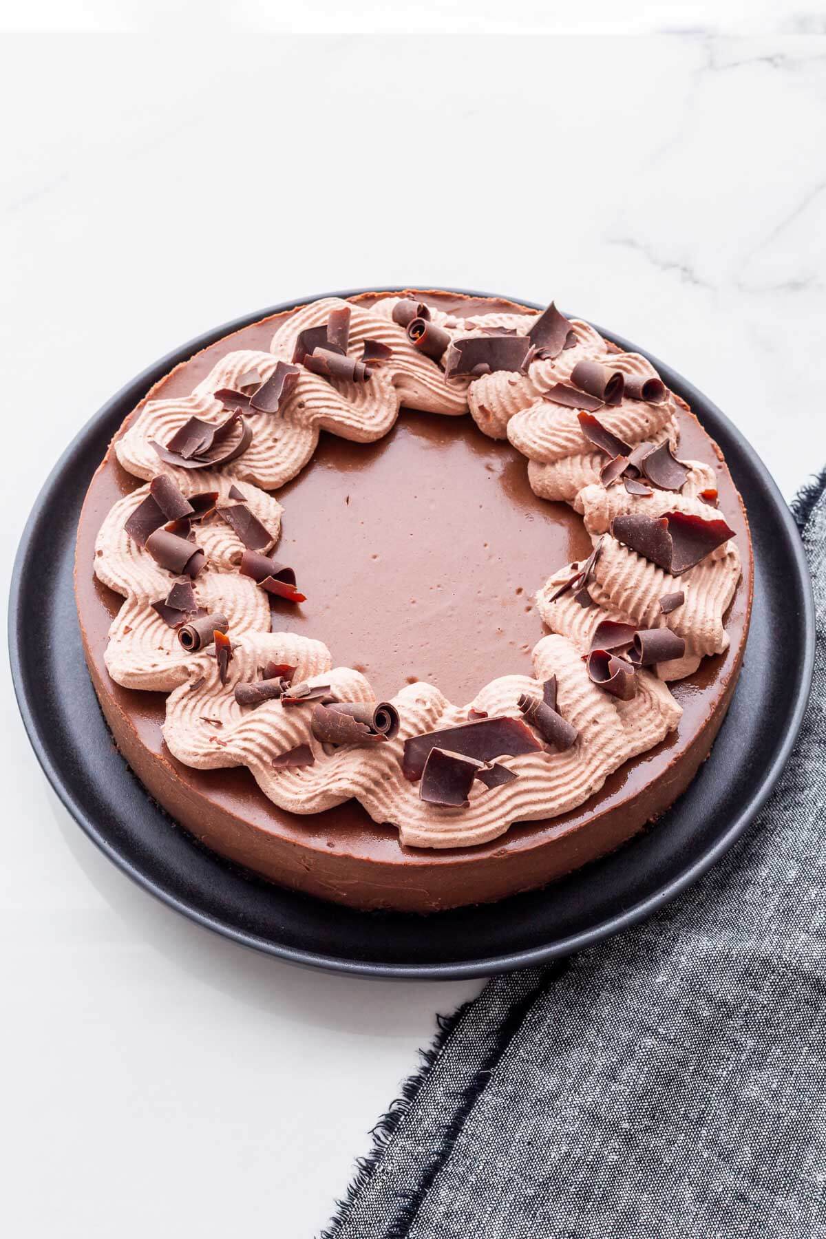 A 9-inch chocolate cheesecake decorated with whipped cream and dark chocolate curls.