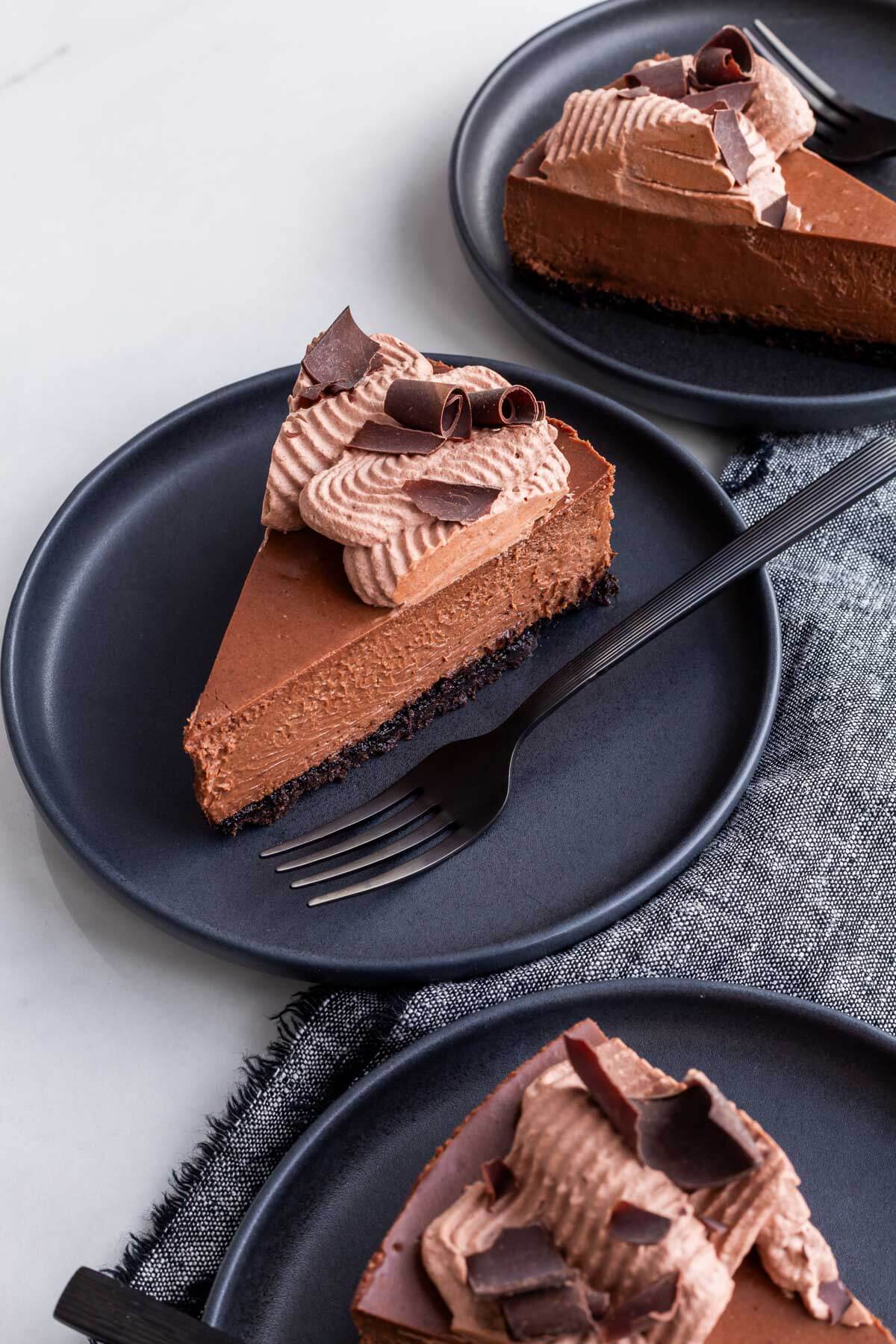 Slices of creamy dark chocolate cheesecake decorated with cocoa whipped cream and shards of dark chocolate.