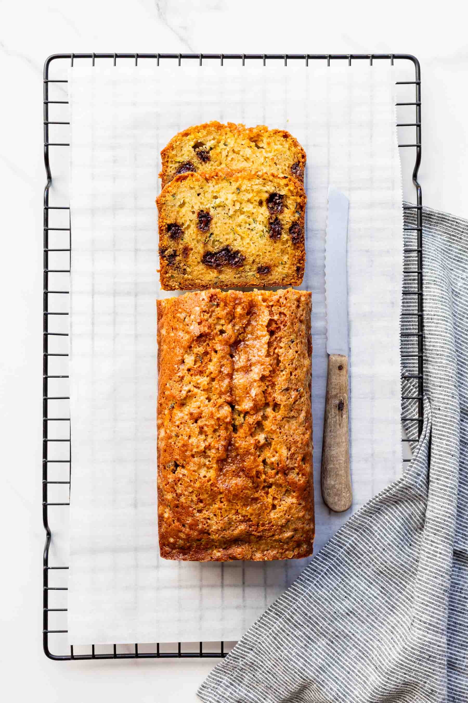 Slicing into a zucchini bread with chocolate chips using a serrated knife.