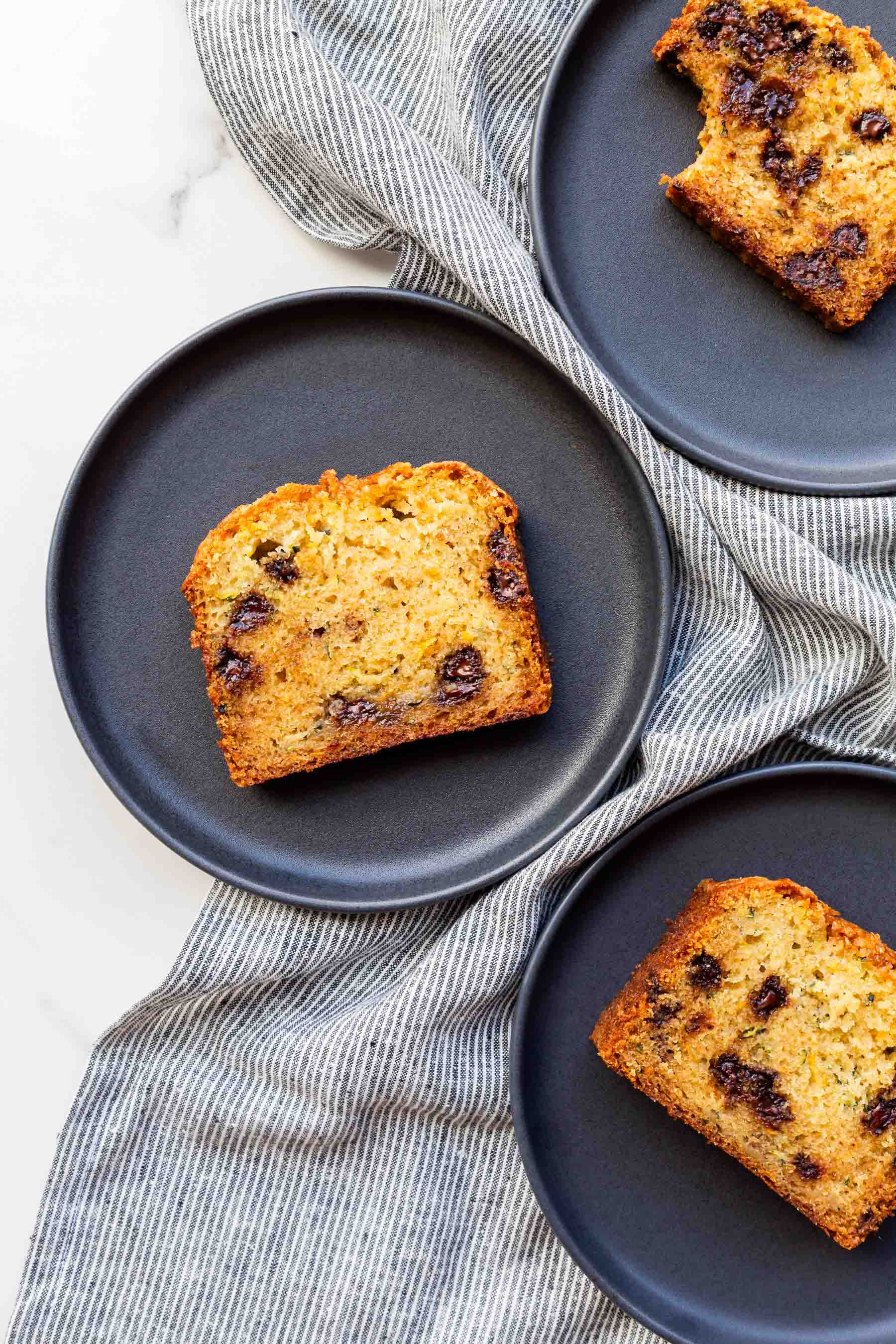 Slices of homemade moist zucchini bread with chocolate chips served on black dessert plates.