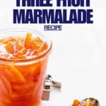 An open jar of marmalade to show the texture with slices of citrus peel and bright orange colour.