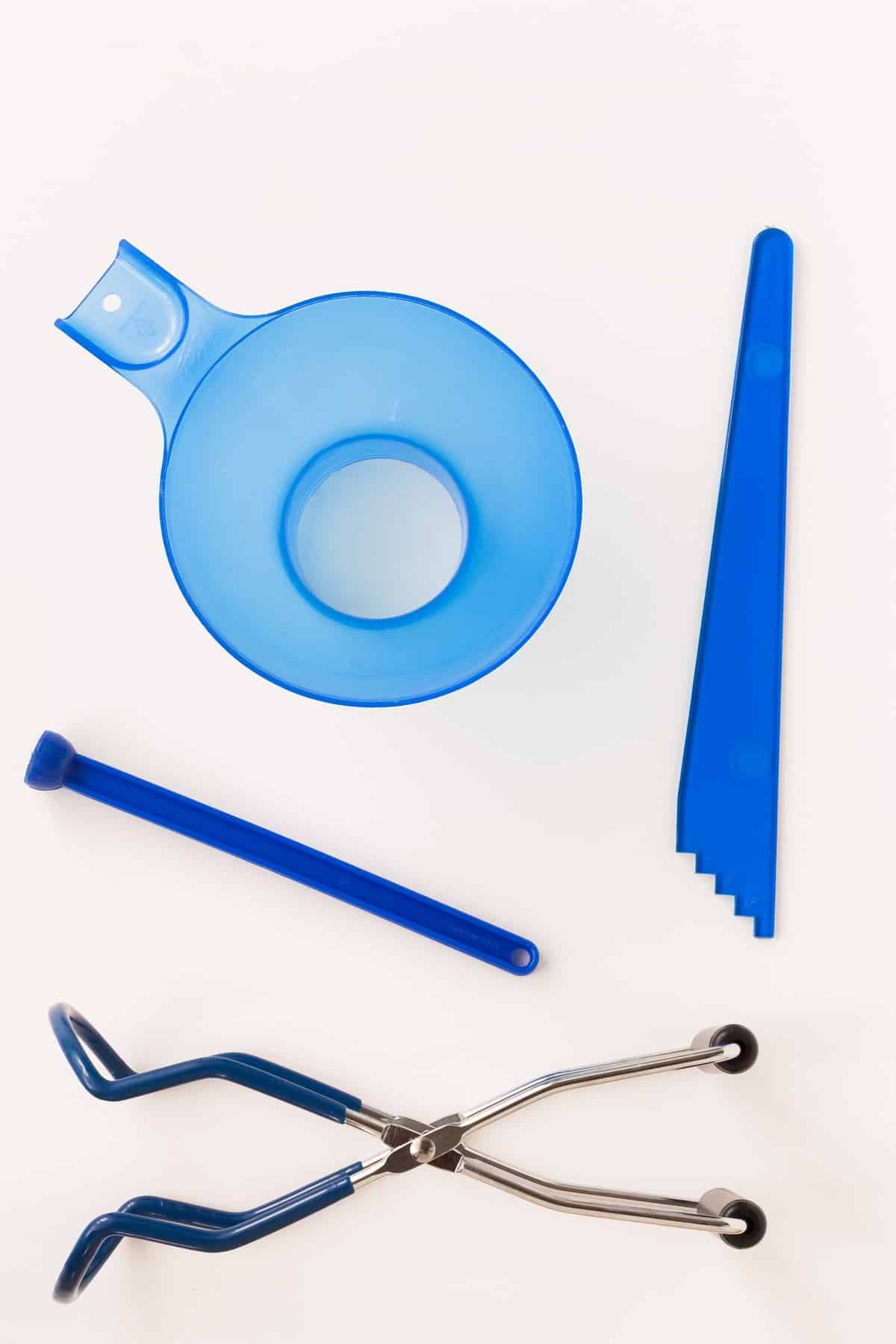 A kit of four tools for home canning, including a non-reactive, heatsafe funnel, a bubble remover with a ruler to measure headspace, a lid lifter and a jar lifter.