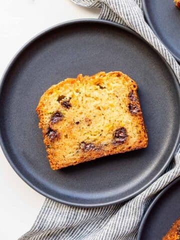 A slice of homemade moist zucchini bread with chocolate chips served on a black dessert plate.