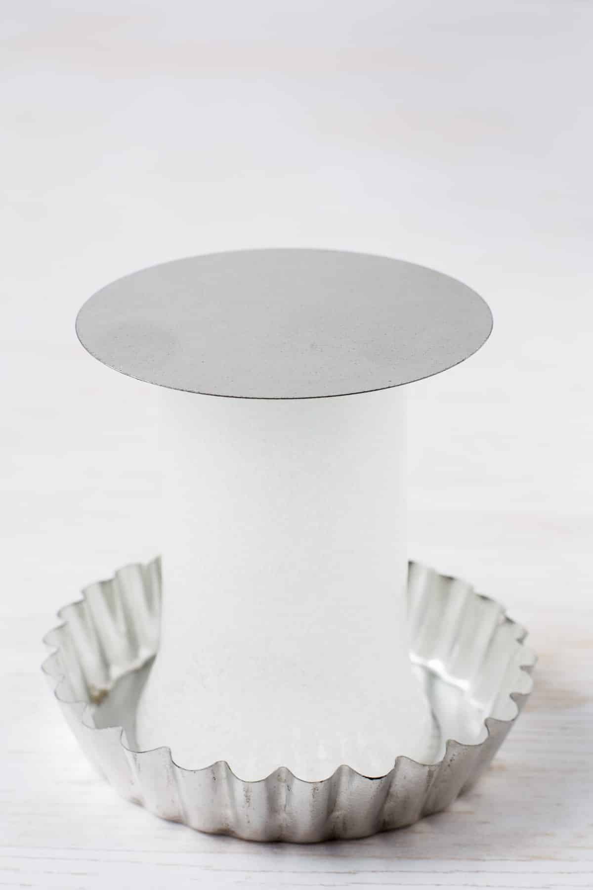 Using a shot glass to separate tart ring from tart pan base in order to demonstrate how to easily remove a tart from a tart pan.