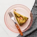 A slice of pumpkin seed cake on a pink glass dessert plate.
