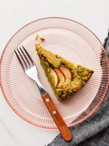 A slice of pumpkin seed cake on a pink glass dessert plate.