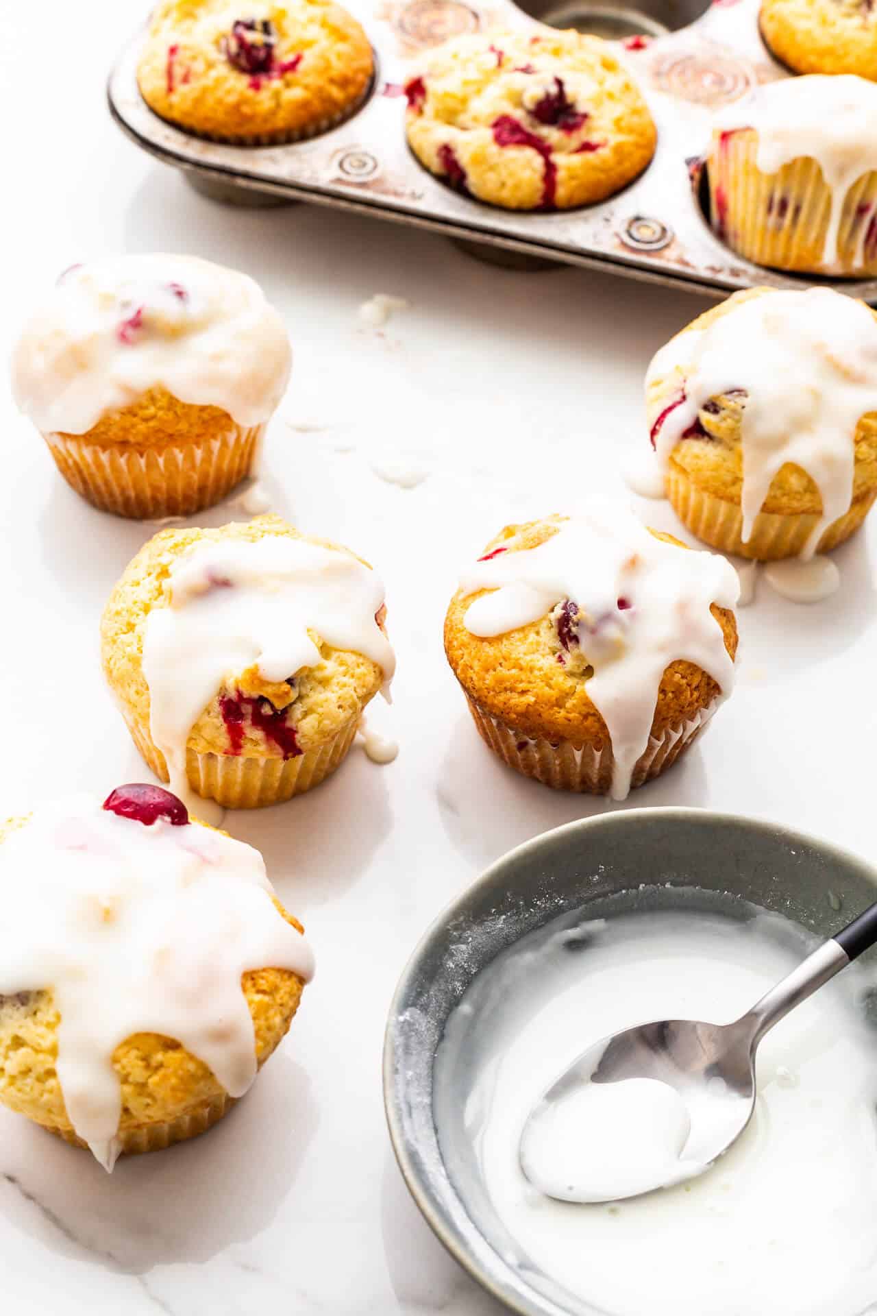 Glazing lemon cranberry muffins with a lemon icing using a spoon.